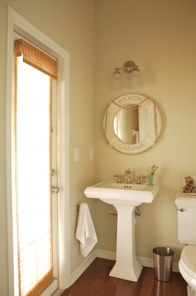 Inredning av ett maritimt litet toalett, med en toalettstol med separat cisternkåpa, beige väggar, mörkt trägolv, ett piedestal handfat och brunt golv