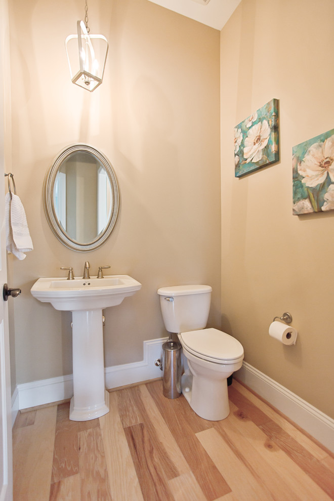 Esempio di un bagno di servizio classico di medie dimensioni con WC a due pezzi, pareti beige, parquet chiaro e lavabo a colonna