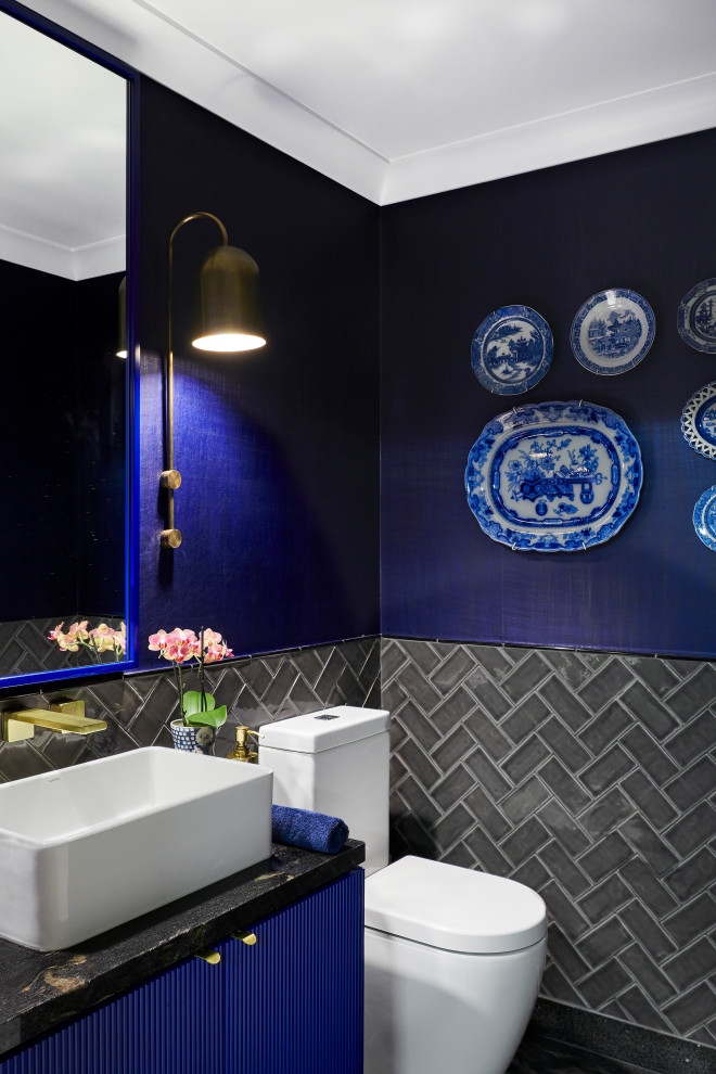 Источник вдохновения для домашнего уюта: туалет среднего размера в стиле фьюжн с фасадами с филенкой типа жалюзи, синими фасадами, унитазом-моноблоком, серой плиткой, плиткой кабанчик, белыми стенами, полом из терраццо, настольной раковиной, столешницей из гранита, серым полом, черной столешницей, напольной тумбой и обоями на стенах
