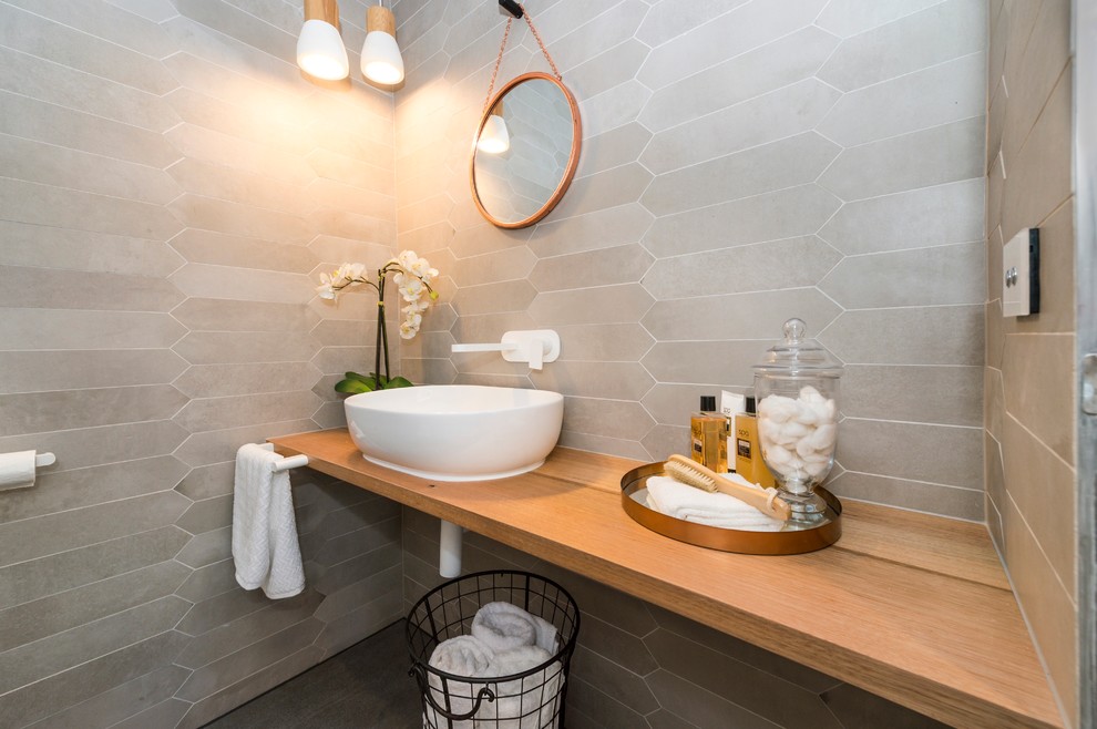 Mid-sized trendy gray tile and stone tile ceramic tile powder room photo in Canberra - Queanbeyan with a wall-mount toilet, white walls, a vessel sink and wood countertops
