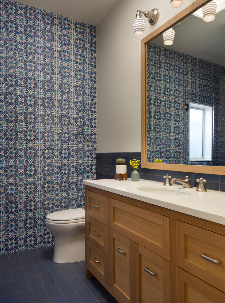 サンフランシスコにあるラグジュアリーな広いトランジショナルスタイルのおしゃれなトイレ・洗面所 (青いタイル、アンダーカウンター洗面器、セラミックタイル、セラミックタイルの床、青い床、落し込みパネル扉のキャビネット、淡色木目調キャビネット、一体型トイレ	、マルチカラーの壁、ソープストーンの洗面台、白い洗面カウンター、アクセントウォール) の写真