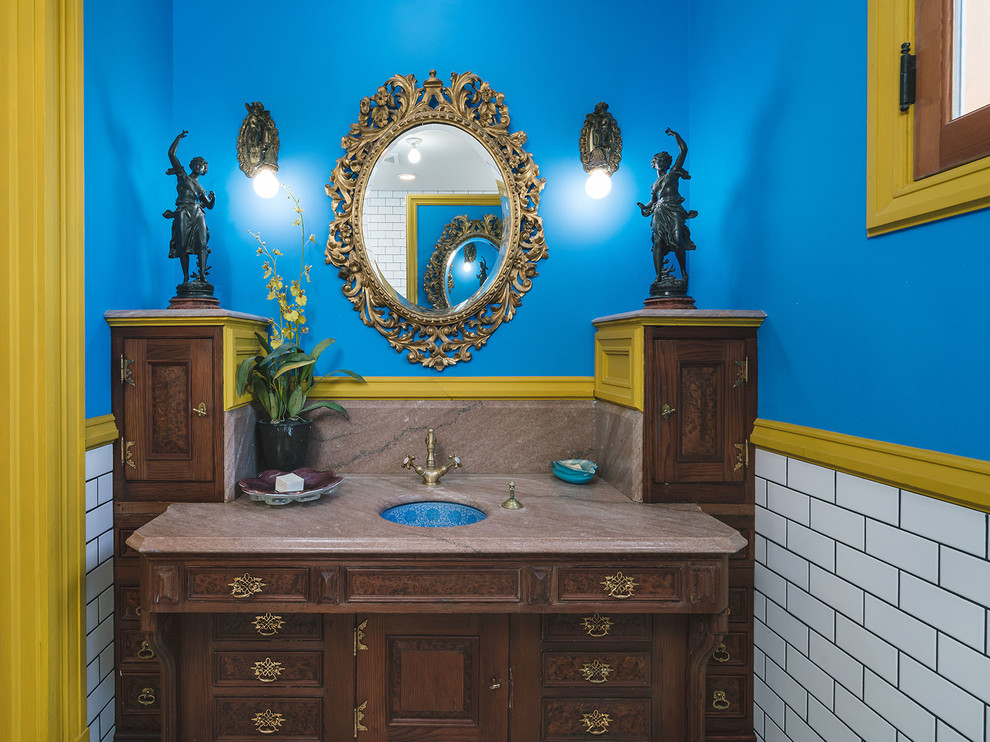 Cette image montre un WC et toilettes victorien en bois foncé avec un placard en trompe-l'oeil, un mur bleu, un lavabo encastré et un plan de toilette marron.