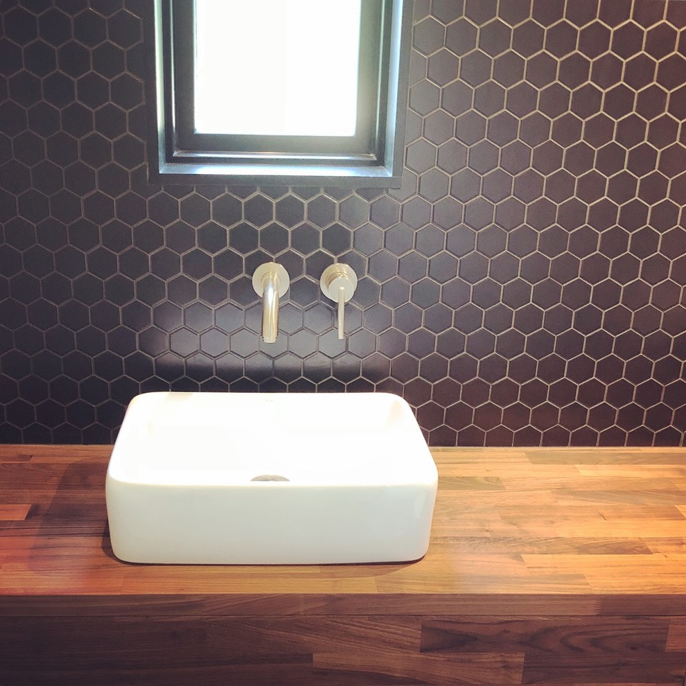 Exempel på ett modernt toalett, med skåp i mellenmörkt trä, svart kakel, mosaik, svarta väggar, betonggolv, ett fristående handfat, träbänkskiva och grått golv