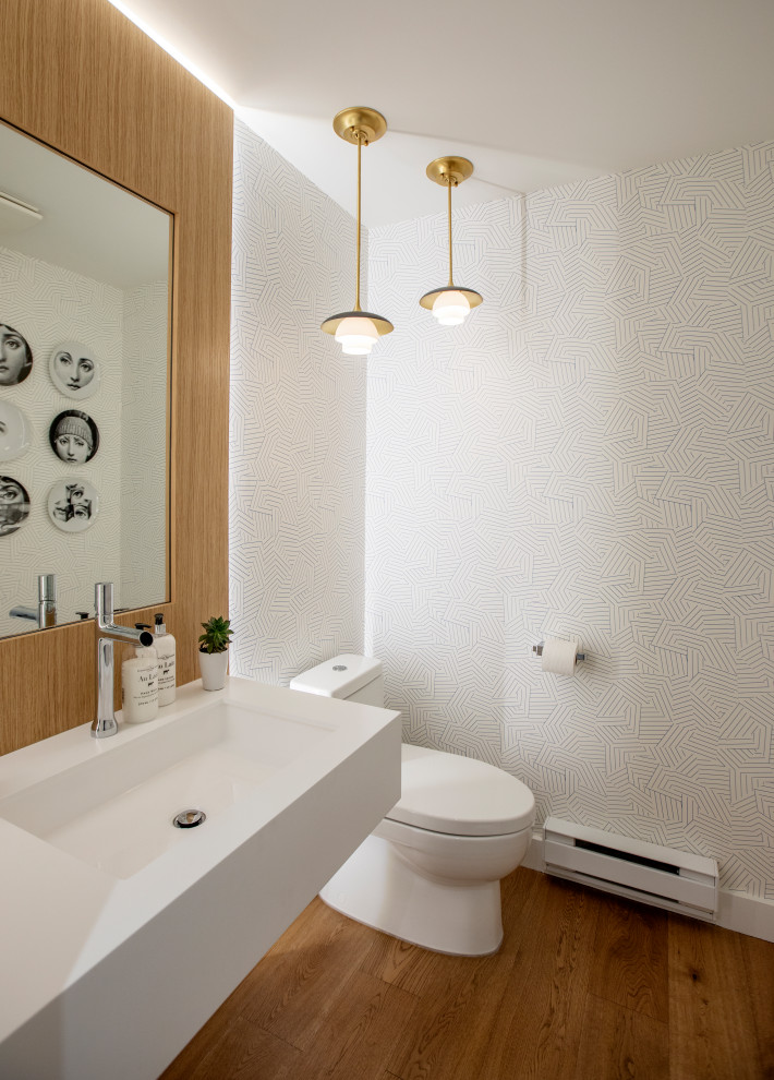 Esempio di un bagno di servizio minimal con pareti bianche, pavimento in legno massello medio, lavabo integrato, pavimento marrone, top bianco e carta da parati