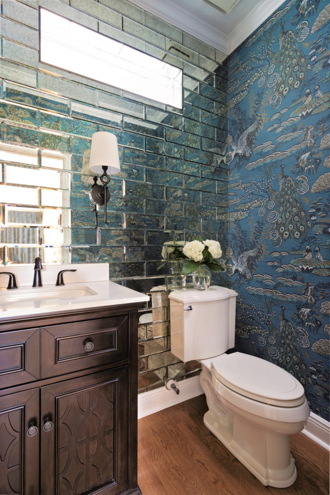 Example of a transitional mirror tile wallpaper and medium tone wood floor powder room design in Orlando with recessed-panel cabinets, dark wood cabinets, a two-piece toilet, multicolored walls, an undermount sink, quartz countertops, white countertops and a built-in vanity