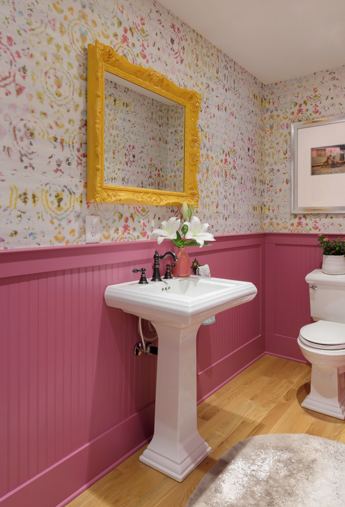 Mid-sized transitional light wood floor and brown floor powder room photo in Portland with a two-piece toilet, multicolored walls, a pedestal sink, solid surface countertops and white countertops