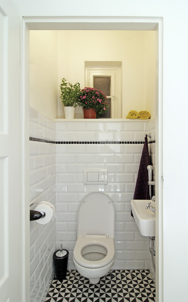 Modelo de aseo bohemio pequeño con lavabo suspendido, sanitario de pared, baldosas y/o azulejos blancas y negros, paredes blancas, suelo de baldosas de cerámica y baldosas y/o azulejos de cemento