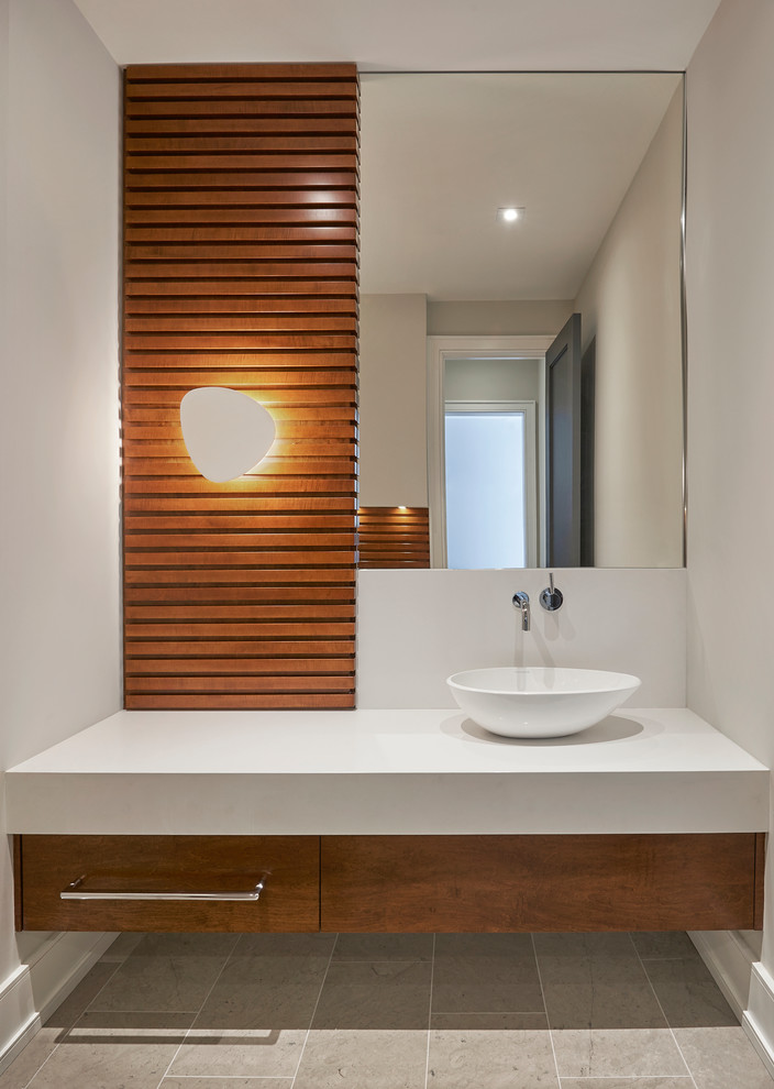 Réalisation d'un WC et toilettes design en bois brun de taille moyenne avec un placard à porte plane, un mur blanc, un sol en carrelage de porcelaine, une vasque, un plan de toilette en surface solide et un sol gris.