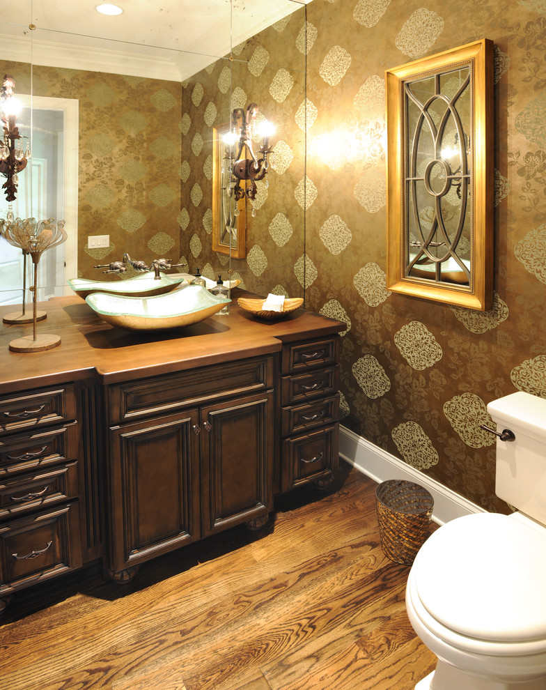 Bild på ett vintage brun brunt toalett, med luckor med infälld panel, skåp i mörkt trä, en toalettstol med separat cisternkåpa, bruna väggar, mellanmörkt trägolv, ett fristående handfat, träbänkskiva och brunt golv