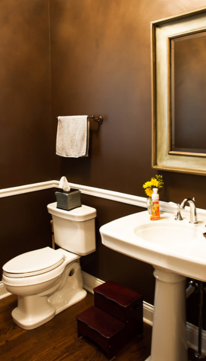 Inredning av ett klassiskt mellanstort toalett, med en toalettstol med separat cisternkåpa, bruna väggar, mellanmörkt trägolv, ett piedestal handfat och brunt golv