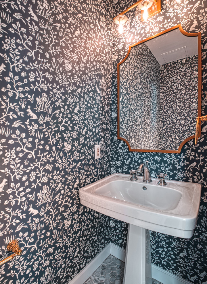 Bild på ett litet funkis toalett, med en toalettstol med hel cisternkåpa, blå väggar, mosaikgolv, ett piedestal handfat och flerfärgat golv