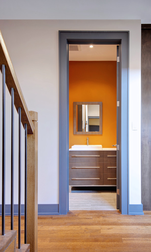 Cette image montre un WC et toilettes design en bois brun de taille moyenne avec une vasque, un placard à porte plane, un plan de toilette en quartz modifié, un mur orange, un sol en carrelage de porcelaine, WC à poser et un carrelage gris.