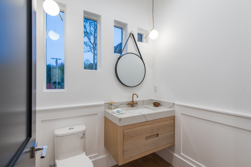 Photo of a medium sized contemporary cloakroom in Los Angeles with flat-panel cabinets, light wood cabinets, a one-piece toilet, white walls, a submerged sink, brown floors, grey worktops, a floating vanity unit and wainscoting.