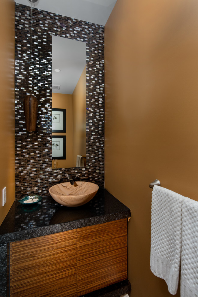 This is an example of a medium sized contemporary cloakroom in Toronto with flat-panel cabinets, medium wood cabinets, a two-piece toilet, brown tiles, glass tiles, brown walls, ceramic flooring, a vessel sink, granite worktops and beige floors.