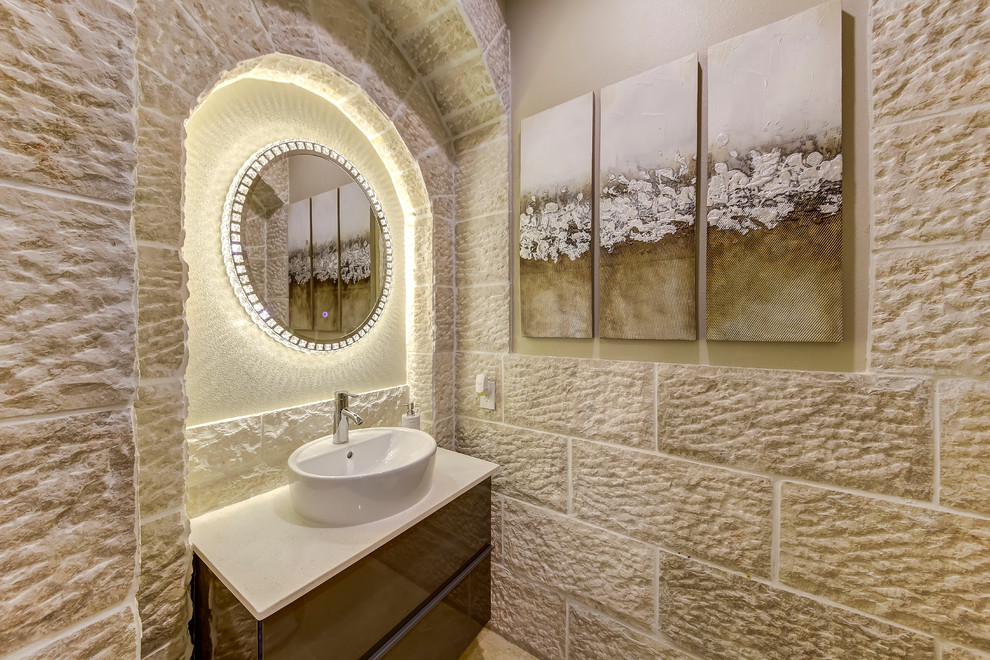 Пример оригинального дизайна: туалет среднего размера в средиземноморском стиле с плоскими фасадами, коричневыми фасадами, бежевой плиткой, каменной плиткой, бежевыми стенами, настольной раковиной, столешницей из известняка и бежевой столешницей