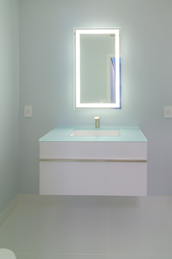 Inspiration pour un petit WC et toilettes design avec un lavabo encastré, un placard à porte plane, des portes de placard blanches, WC séparés, un mur blanc, un sol en carrelage de porcelaine, un plan de toilette en verre et un sol blanc.