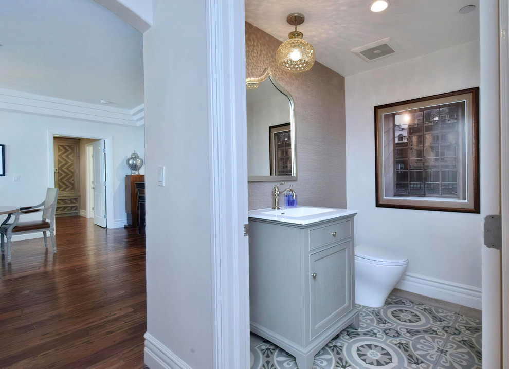 Example of a mid-sized tuscan porcelain tile, multicolored floor and wallpaper powder room design in Los Angeles with shaker cabinets, gray cabinets, a one-piece toilet, gray walls, an integrated sink, solid surface countertops, white countertops and a freestanding vanity