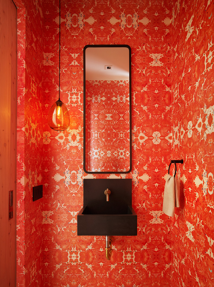 他の地域にあるコンテンポラリースタイルのおしゃれなトイレ・洗面所 (赤い壁、壁付け型シンク、黒い洗面カウンター) の写真