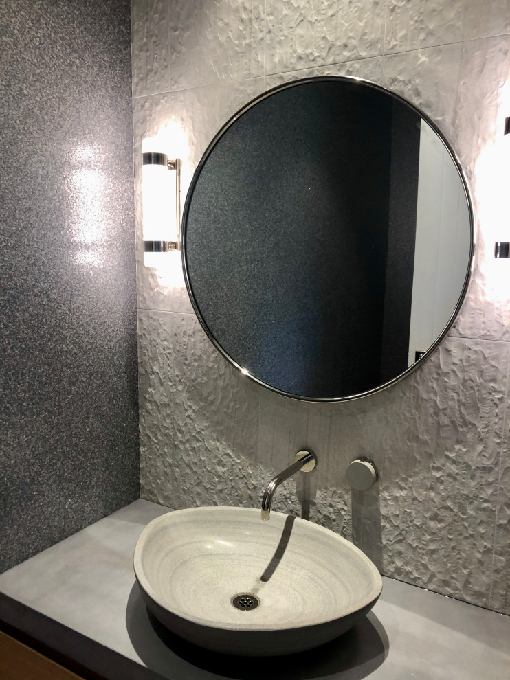 Modern inredning av ett litet grå grått toalett, med släta luckor, beige skåp, en toalettstol med separat cisternkåpa, grå kakel, porslinskakel, grå väggar, ljust trägolv, ett fristående handfat, bänkskiva i betong och beiget golv