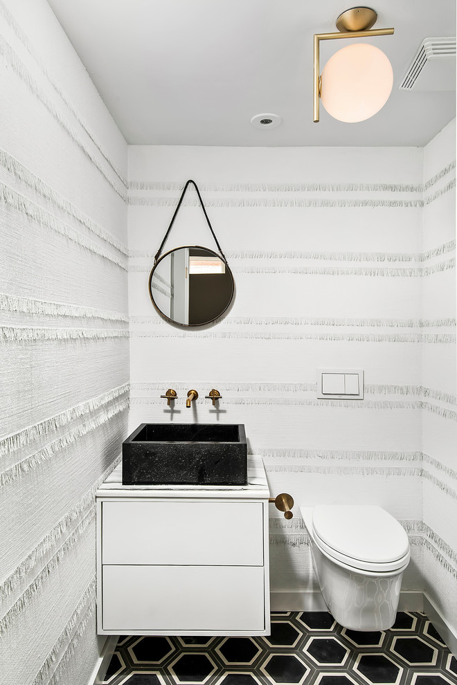 Bild på ett funkis toalett, med ett fristående handfat, släta luckor, vita skåp, en vägghängd toalettstol, vita väggar och flerfärgat golv