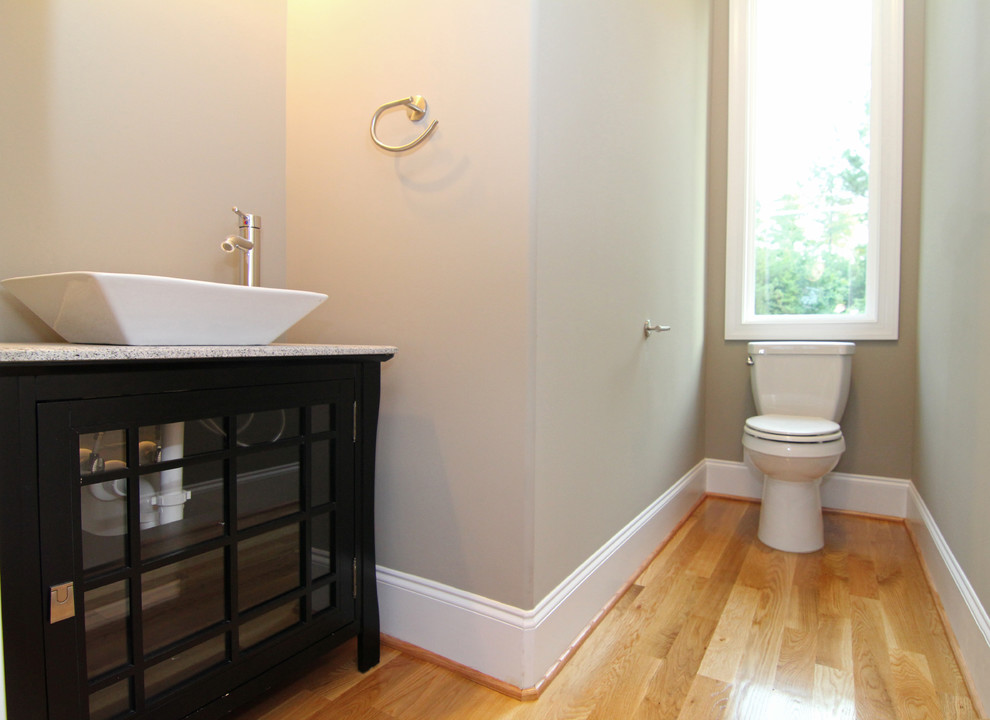 Exempel på ett litet modernt toalett, med ett fristående handfat, luckor med glaspanel, svarta skåp, en toalettstol med hel cisternkåpa, grå väggar och ljust trägolv