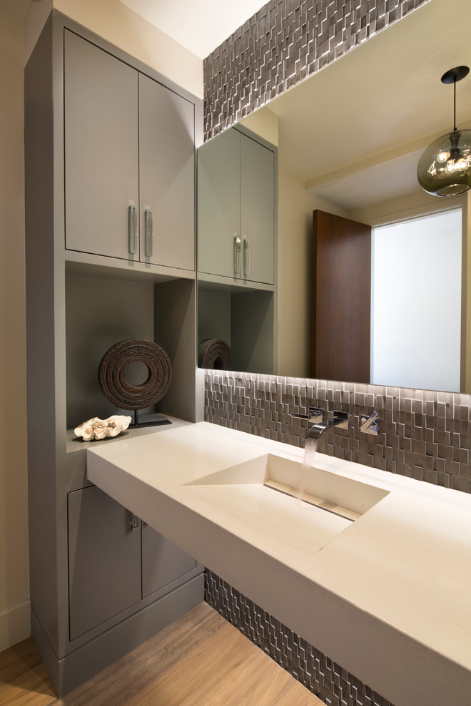 Cette image montre un WC et toilettes design avec un placard à porte plane, des portes de placard grises, un mur beige, parquet clair et un lavabo intégré.