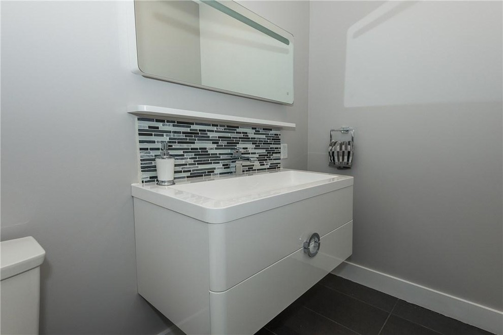 Modern inredning av ett mellanstort toalett, med släta luckor, vita skåp, grå väggar, klinkergolv i keramik, ett integrerad handfat, bänkskiva i akrylsten och grått golv
