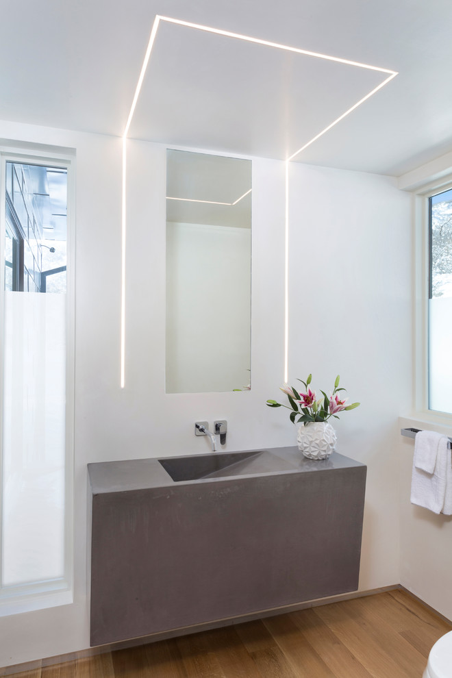 На фото: туалет среднего размера в современном стиле с белыми стенами, светлым паркетным полом, раковиной с несколькими смесителями, столешницей из бетона и коричневым полом с