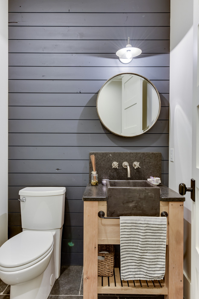 Photo of a small farmhouse cloakroom in Minneapolis with freestanding cabinets, brown cabinets, a two-piece toilet, blue tiles, blue walls, limestone flooring, a built-in sink, granite worktops, blue floors and black worktops.