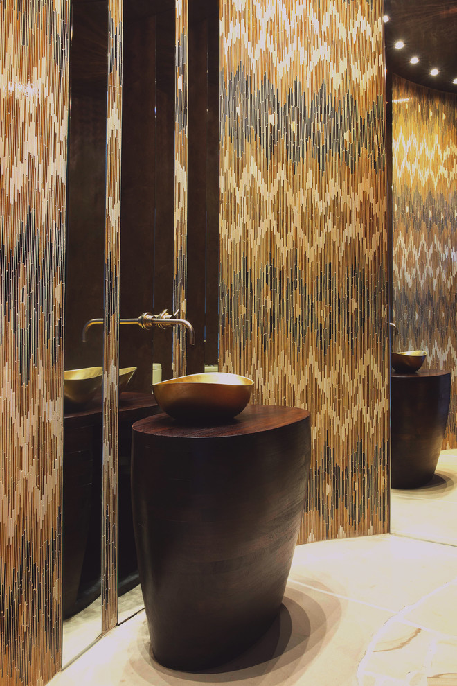 Bild på ett litet funkis brun brunt toalett, med ett fristående handfat, träbänkskiva, flerfärgad kakel, bruna väggar och kalkstensgolv