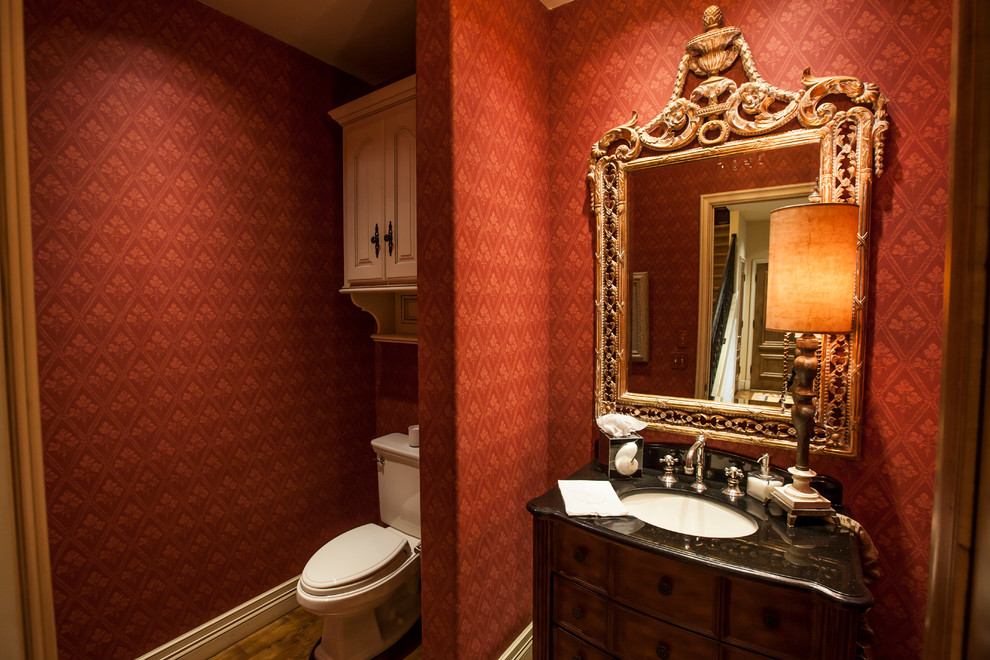 Esempio di un grande bagno di servizio classico con consolle stile comò, ante in legno bruno, WC a due pezzi, pareti rosse, pavimento in legno massello medio, lavabo sottopiano e top in granito