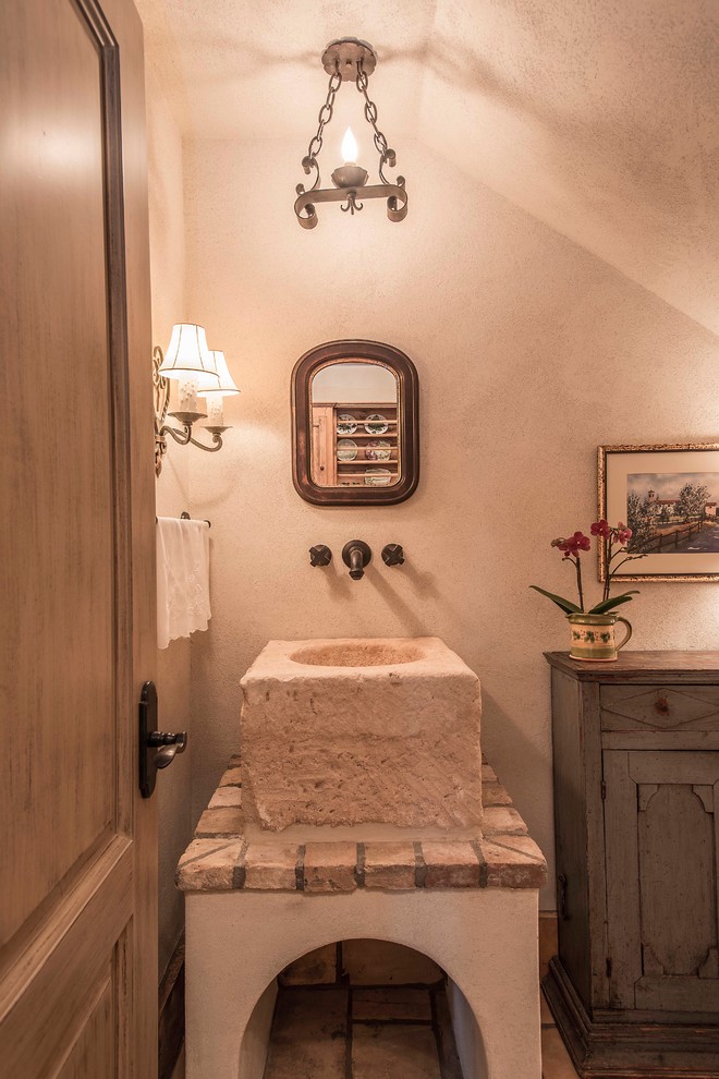Foto på ett litet rustikt toalett, med möbel-liknande, grå skåp, en toalettstol med hel cisternkåpa, flerfärgad kakel, beige väggar, klinkergolv i terrakotta, kaklad bänkskiva och ett fristående handfat