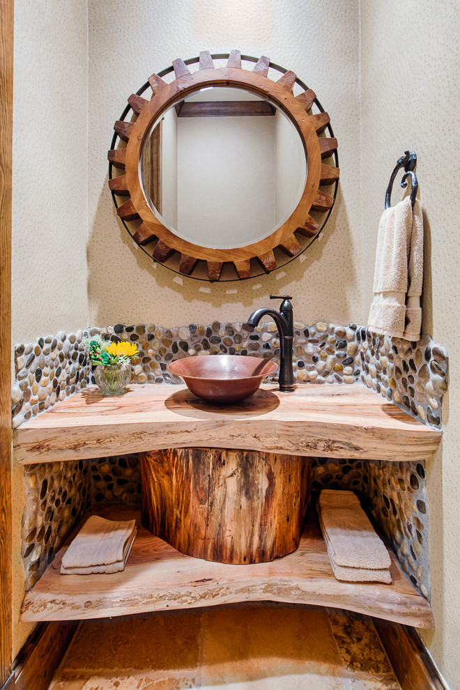Bild på ett stort rustikt beige beige toalett, med ett fristående handfat, öppna hyllor, skåp i mellenmörkt trä, träbänkskiva, beige kakel, kakel i småsten, beige väggar och kalkstensgolv