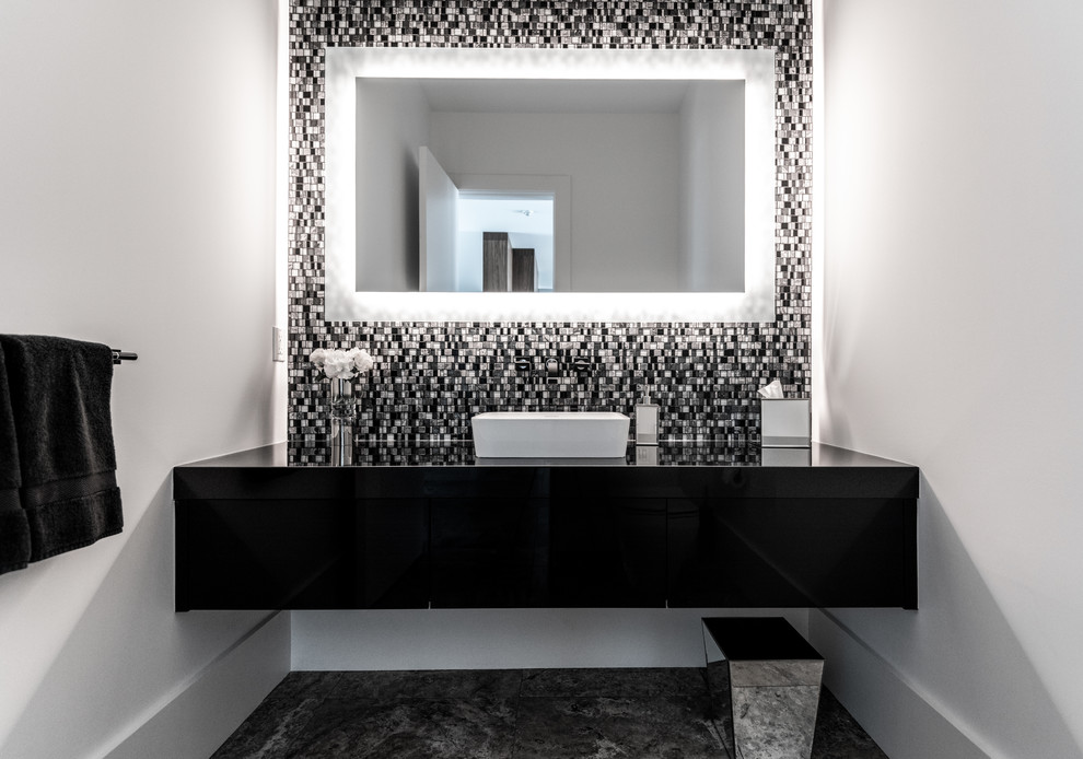 Aménagement d'un WC et toilettes contemporain avec un placard à porte plane, des portes de placard noires, un carrelage noir et blanc, mosaïque, un mur blanc, une vasque, un sol multicolore et un plan de toilette noir.