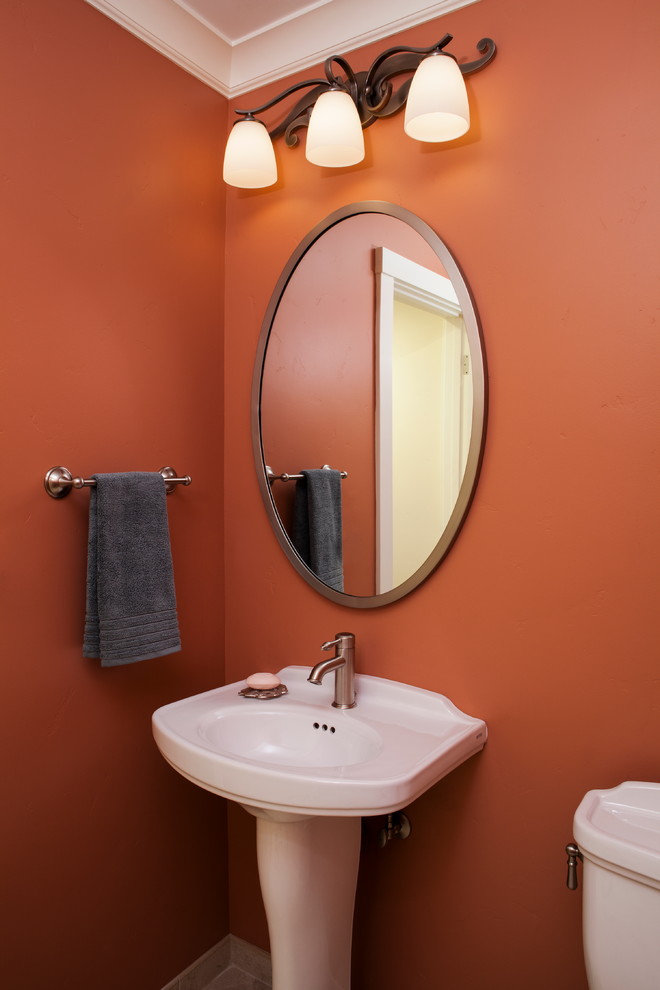 Modelo de aseo de estilo americano pequeño con sanitario de una pieza, lavabo con pedestal, suelo de baldosas de porcelana y parades naranjas