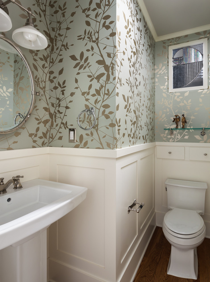 Inredning av ett amerikanskt litet toalett, med skåp i shakerstil, vita skåp, en toalettstol med separat cisternkåpa, gröna väggar, mellanmörkt trägolv, ett piedestal handfat och brunt golv