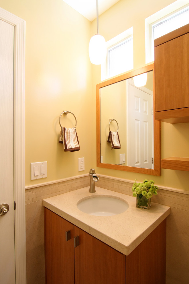 Inspiration för ett litet amerikanskt toalett, med släta luckor, skåp i mellenmörkt trä, beige kakel, gula väggar, ett undermonterad handfat, bänkskiva i kalksten och kakelplattor