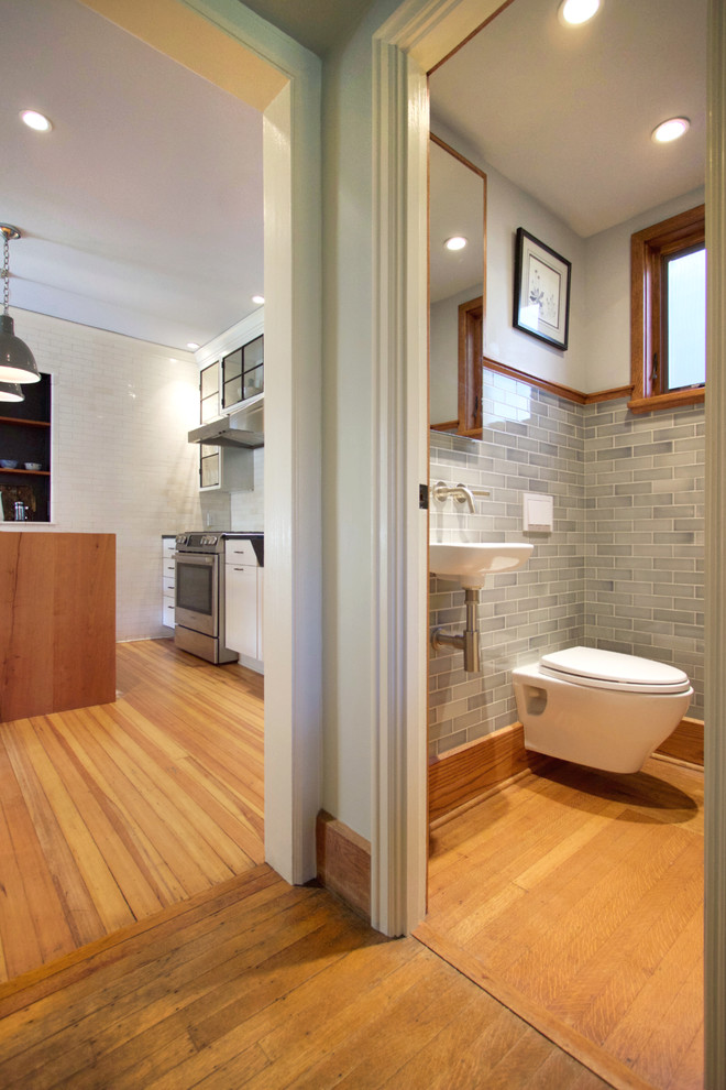 Cette image montre un petit WC suspendu craftsman avec un carrelage gris, un carrelage métro, un mur gris, un sol en bois brun et un lavabo suspendu.
