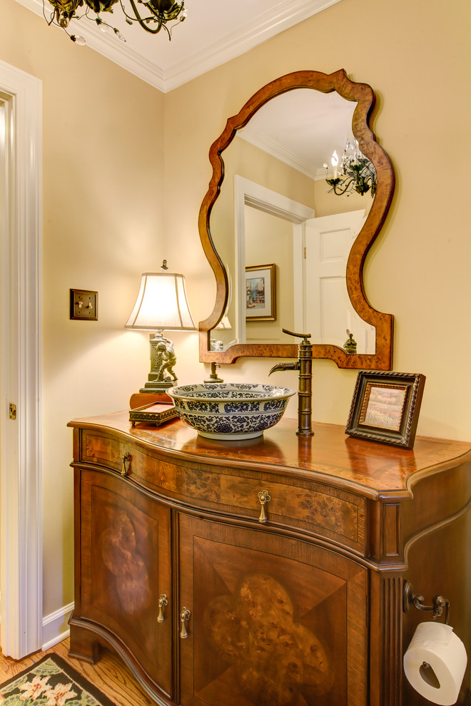 Example of a mid-sized classic light wood floor powder room design in Raleigh with furniture-like cabinets, dark wood cabinets, beige walls, a vessel sink and wood countertops