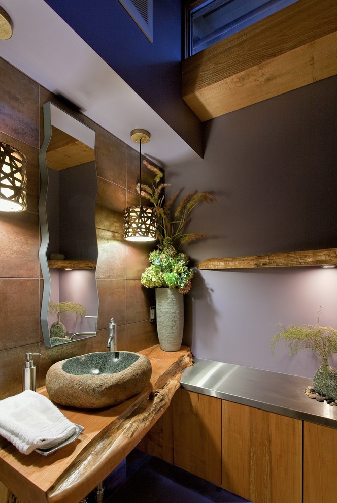 Modern inredning av ett brun brunt toalett, med ett fristående handfat, släta luckor, skåp i mellenmörkt trä, bänkskiva i rostfritt stål, brun kakel, porslinskakel och lila väggar