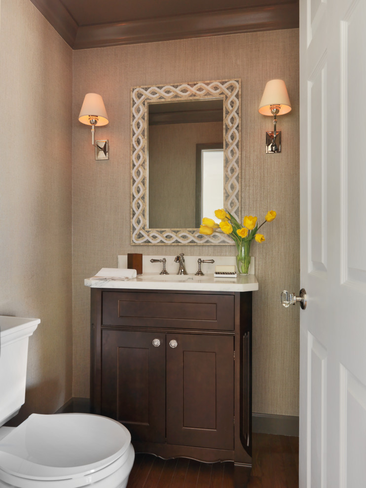 Exemple d'un WC et toilettes chic en bois foncé avec un placard avec porte à panneau encastré, un mur beige, un sol en bois brun et un plan de toilette en marbre.