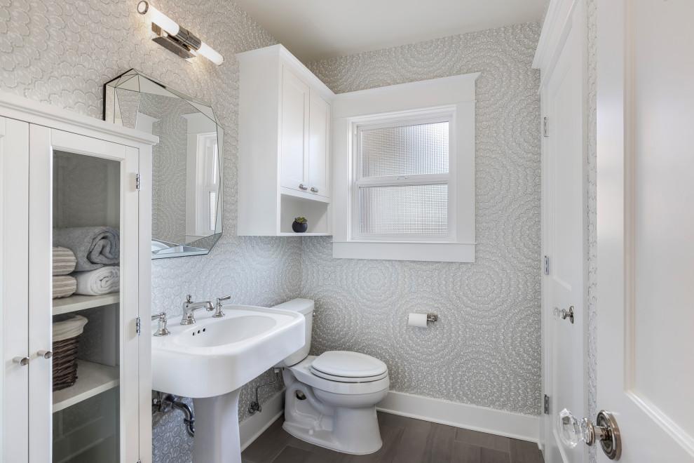 На фото: большой туалет в стиле неоклассика (современная классика) с серыми стенами, раковиной с пьедесталом, коричневым полом и обоями на стенах с