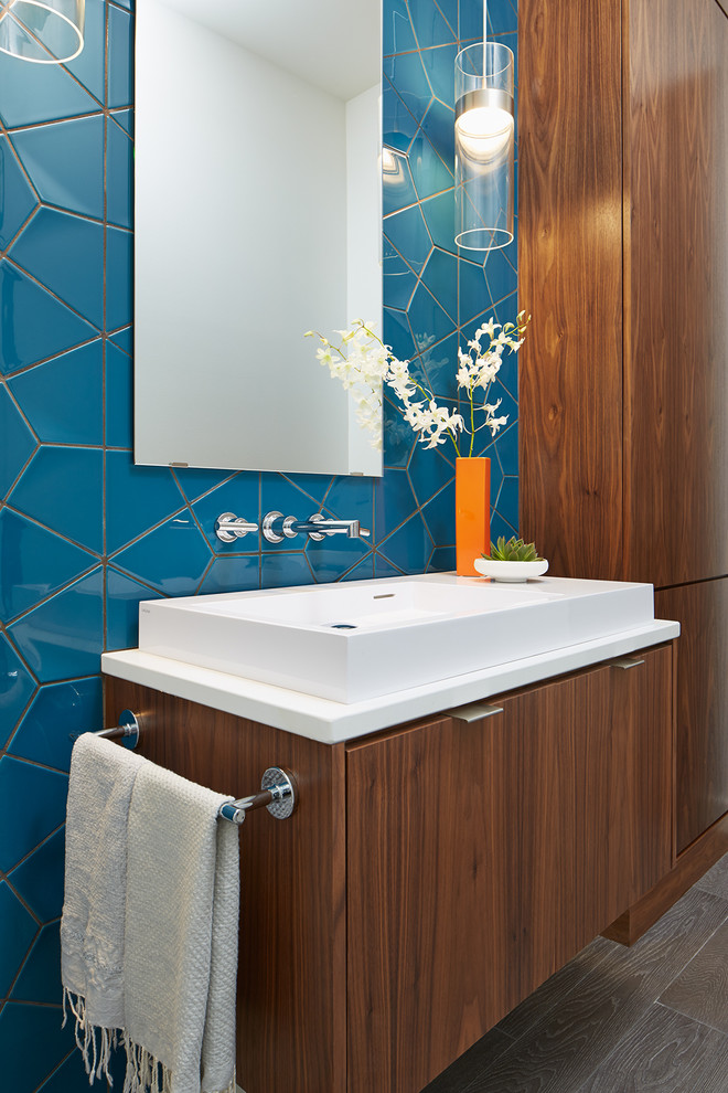 Idee per un bagno di servizio design con ante lisce, ante in legno bruno, top in superficie solida, piastrelle in ceramica, lavabo a bacinella, piastrelle blu e top bianco