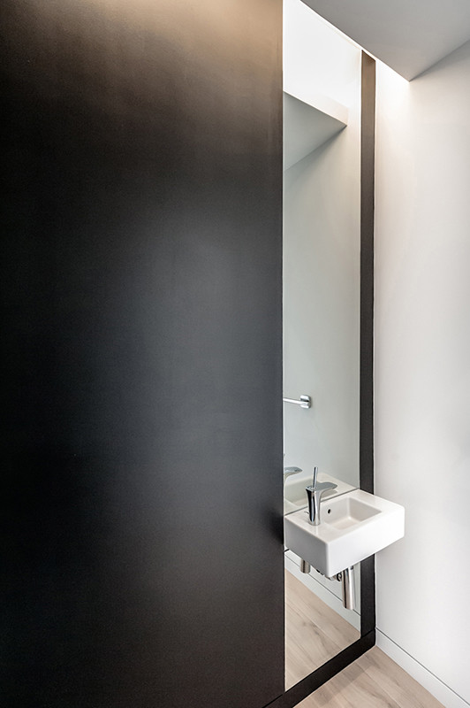 サンフランシスコにある高級な小さなモダンスタイルのおしゃれなトイレ・洗面所 (壁付け型シンク、一体型トイレ	、黒い壁、淡色無垢フローリング) の写真