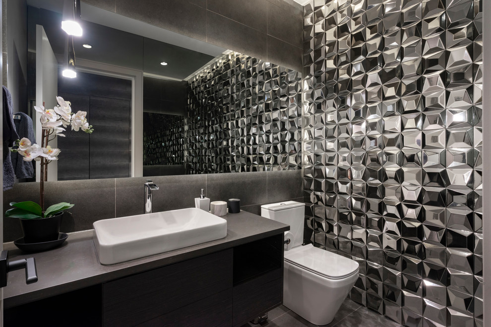 Bild på ett funkis grå grått toalett, med släta luckor, svarta skåp, grå kakel, ett fristående handfat och grått golv