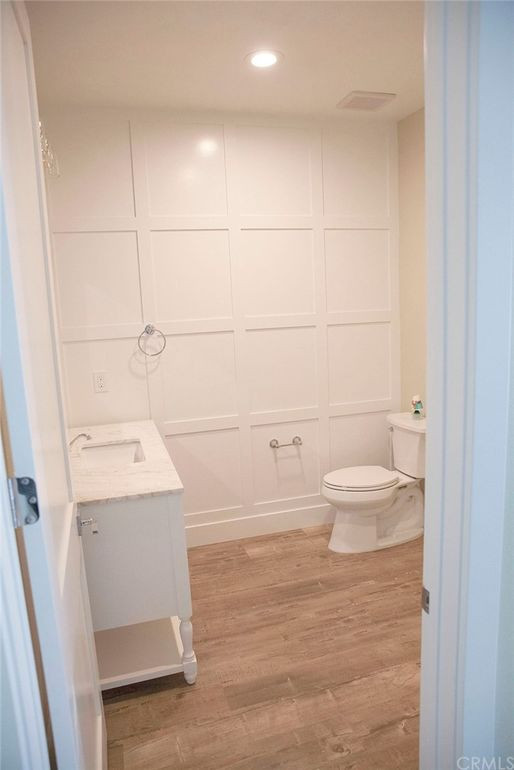 Foto på ett stort lantligt vit toalett, med skåp i shakerstil, vita skåp, en toalettstol med separat cisternkåpa, vit kakel, vita väggar, ett konsol handfat, granitbänkskiva och beiget golv