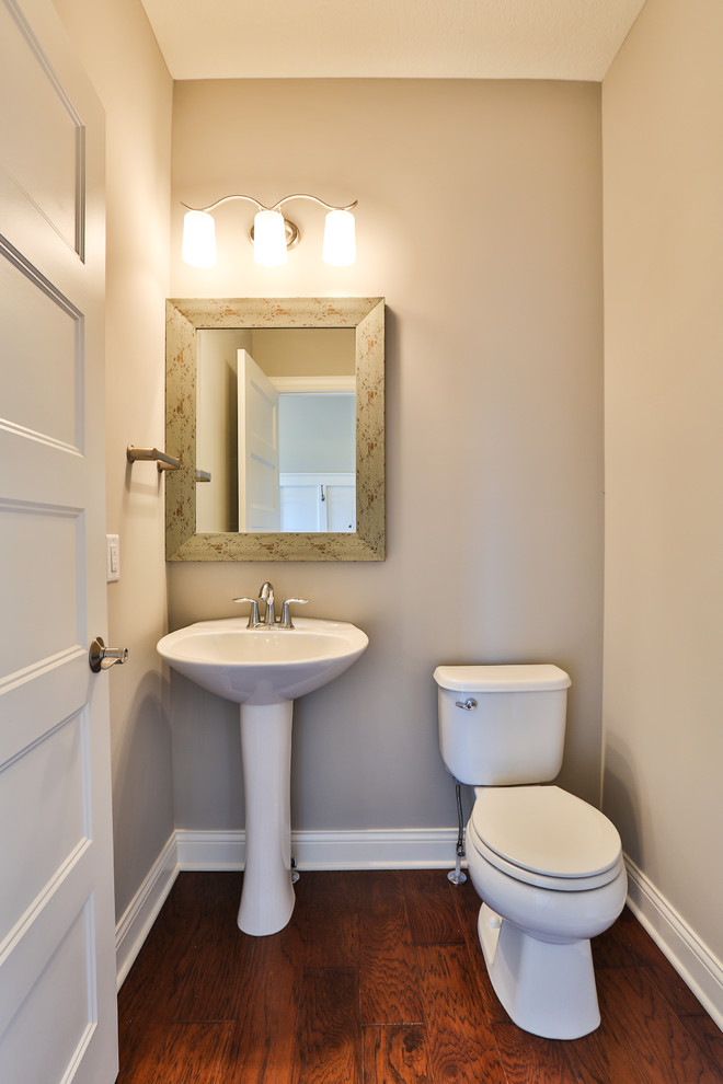 Mittelgroße Gästetoilette mit Sockelwaschbecken, Toilette mit Aufsatzspülkasten, beiger Wandfarbe und braunem Holzboden in Minneapolis