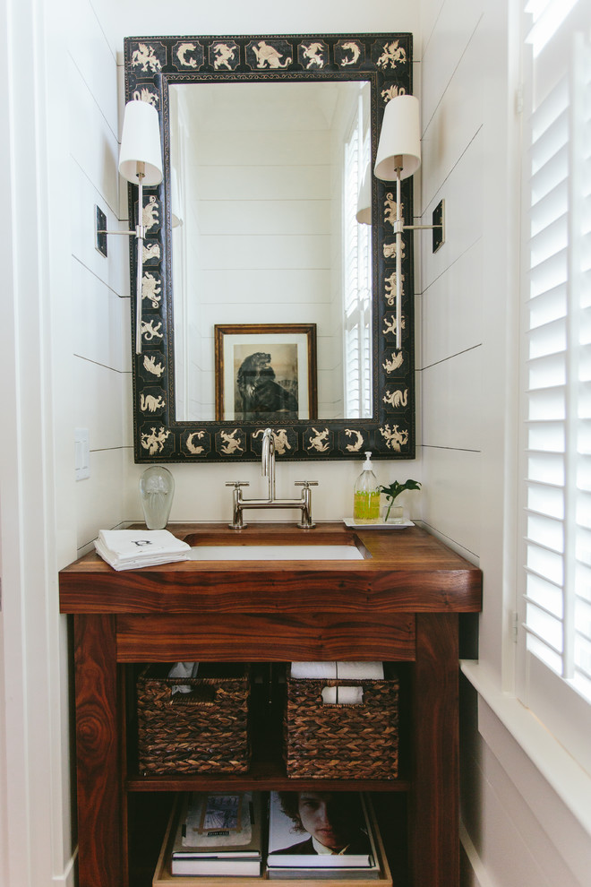 Foto på ett maritimt brun toalett, med öppna hyllor, skåp i mellenmörkt trä, vita väggar, ett undermonterad handfat och träbänkskiva