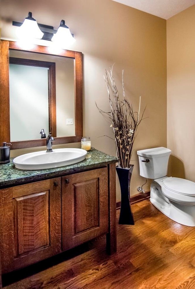 Powder room - mid-sized craftsman medium tone wood floor powder room idea in Omaha with a drop-in sink, raised-panel cabinets, dark wood cabinets, granite countertops, a two-piece toilet and beige walls