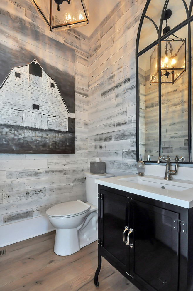 Immagine di un bagno di servizio country con consolle stile comò, ante nere, WC a due pezzi, pareti multicolore, pavimento in legno massello medio, lavabo sottopiano e top bianco